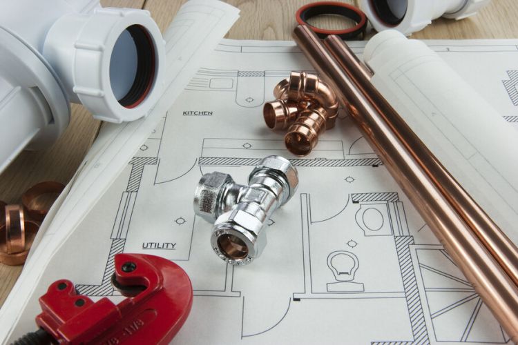 Plumbing tools, copper pipes, and fittings laid out on a home plumbing blueprint plan